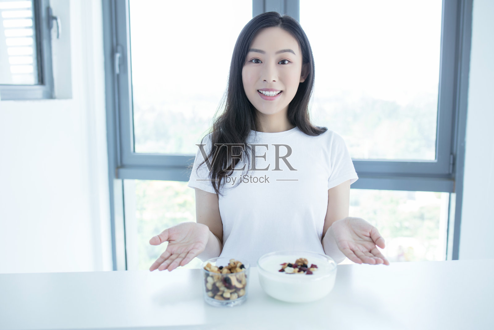 年轻而快乐的女人正在吃新鲜的酸奶和坚果和水果作为早餐照片摄影图片