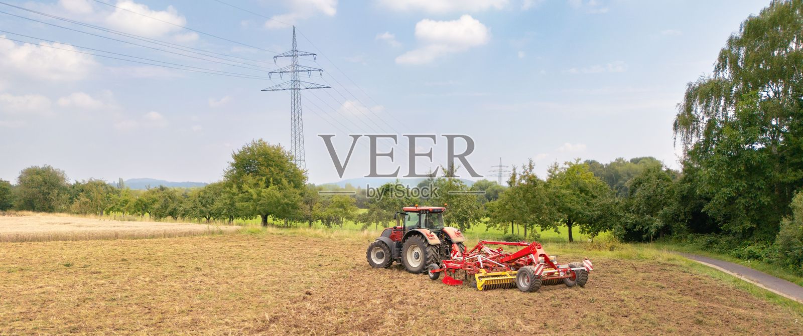 后景一辆红色拖拉机在田野上犁地,在一个阳光明媚的日子里照片摄影图片