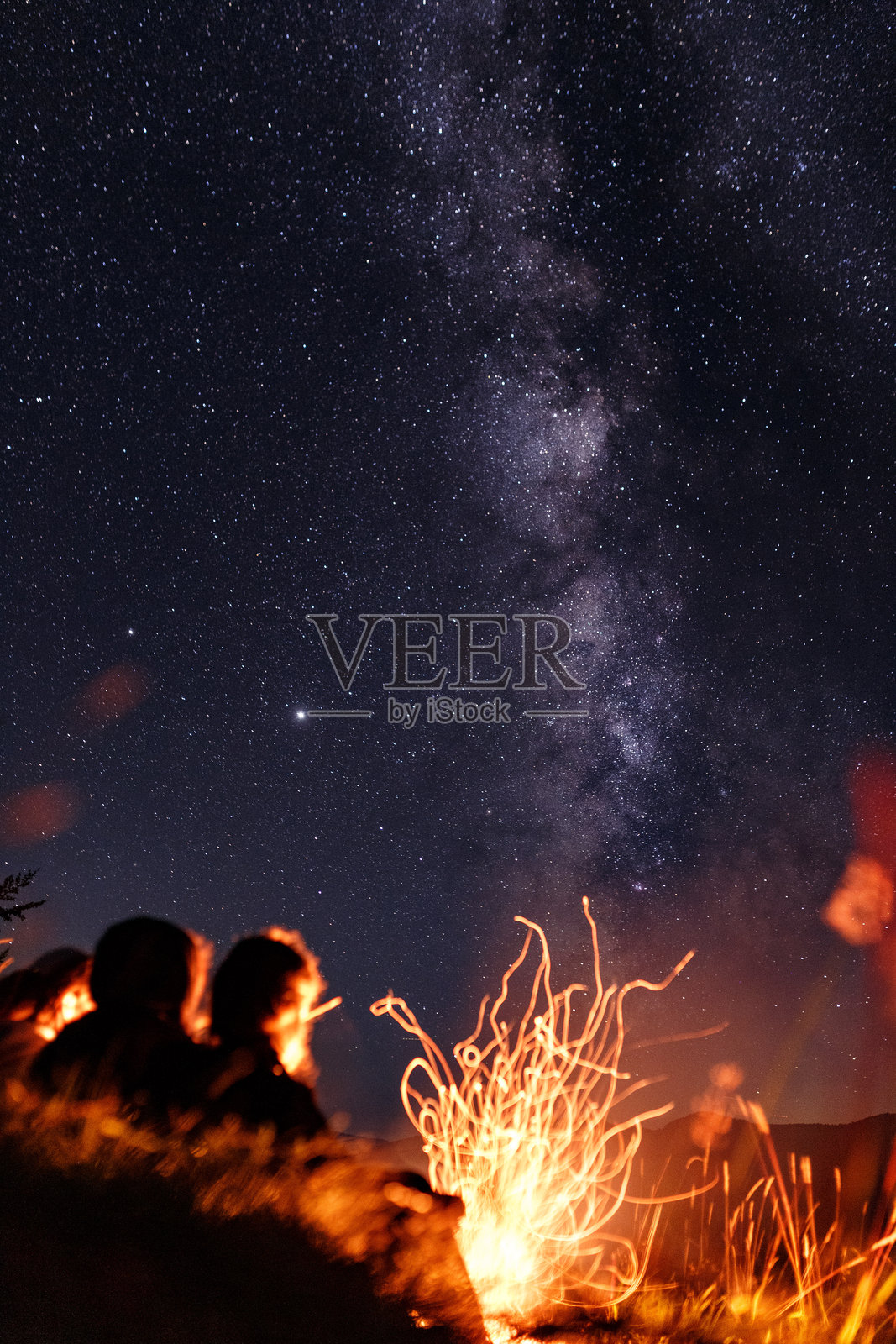 一群朋友坐在银河下的篝火旁照片摄影图片