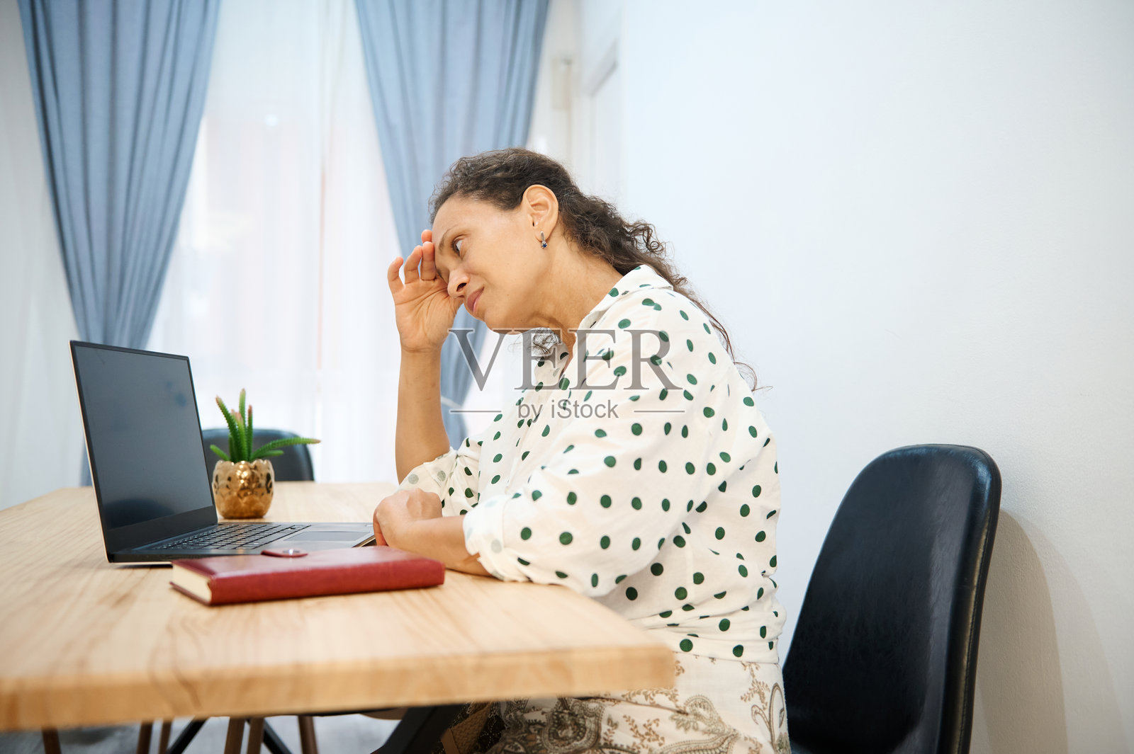 一位穿着圆点衬衫的女士,在家里的办公室里用笔记本电脑工作,看起来很紧张照片摄影图片