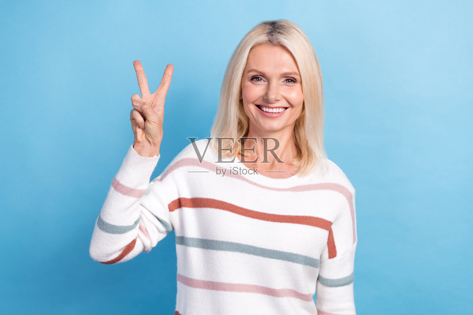 身穿条纹套头衫的女士在蓝色背景上展示V字手势照片摄影图片