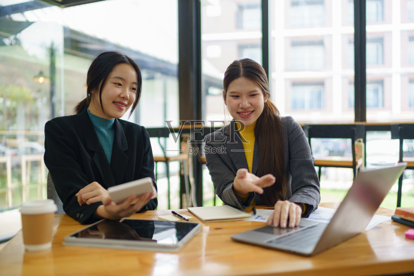 两位年轻的亚洲女商人讨论投资项目工作和规划策略。商务人士在办公室里一起使用笔记本电脑交流。照片摄影图片