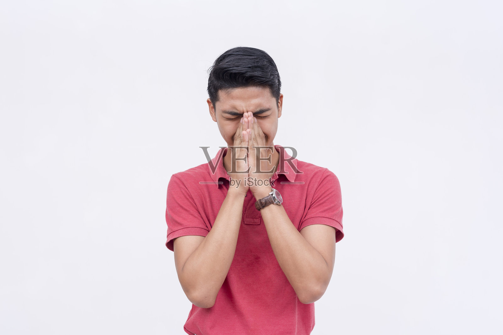 一个男人试图压抑自己的笑声,用手遮住脸,但明显很挣扎。背景为白色。照片摄影图片