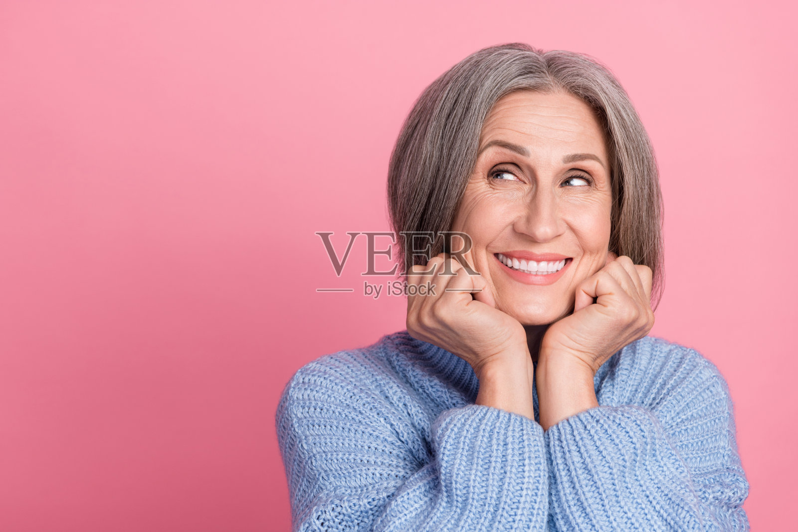 穿着蓝色衣服的美丽积极女性,面带微笑,望向空旷的空间,背景为粉色。照片摄影图片