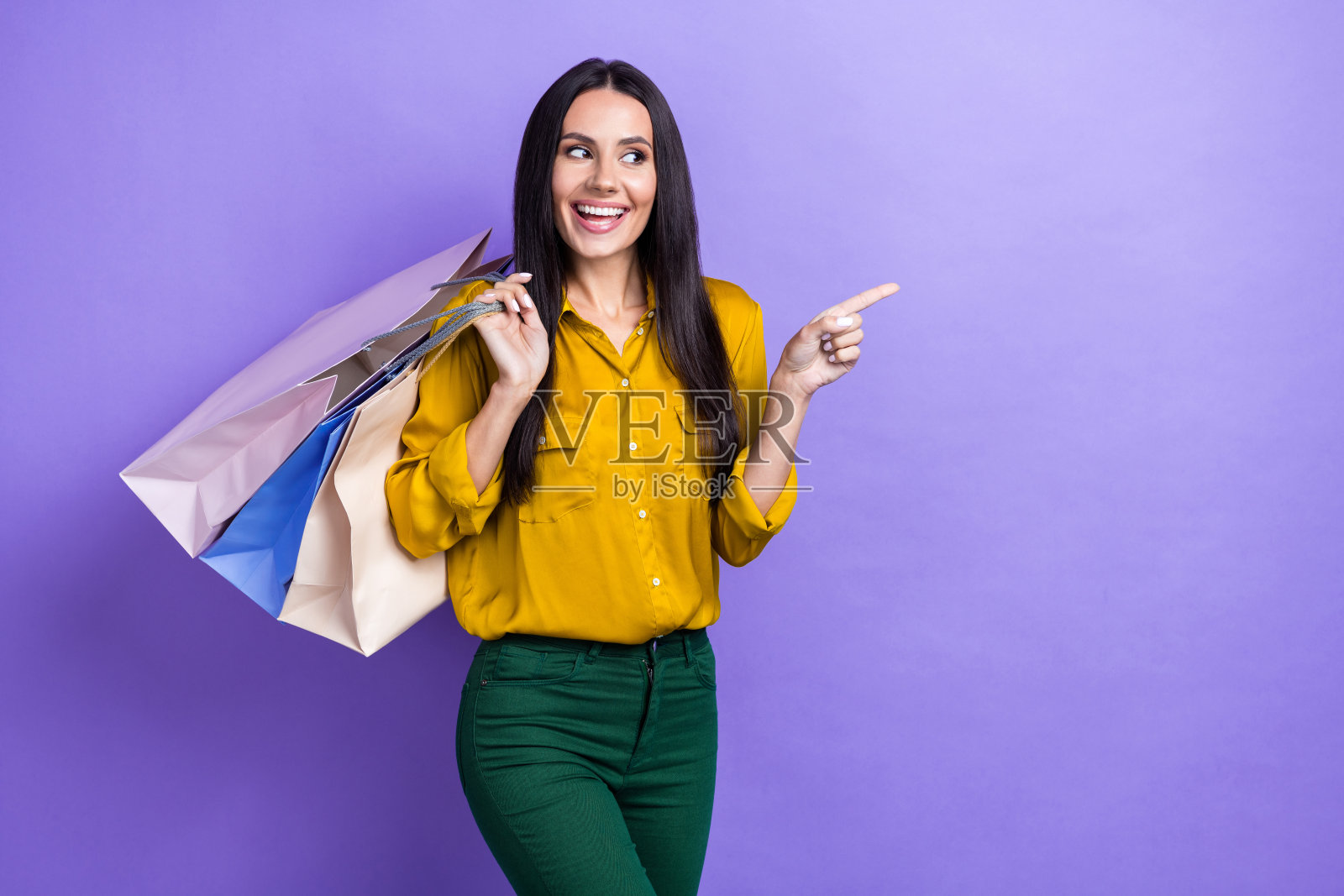 快乐迷人的女孩手持精品袋,直视空白处,背景为紫色。照片摄影图片