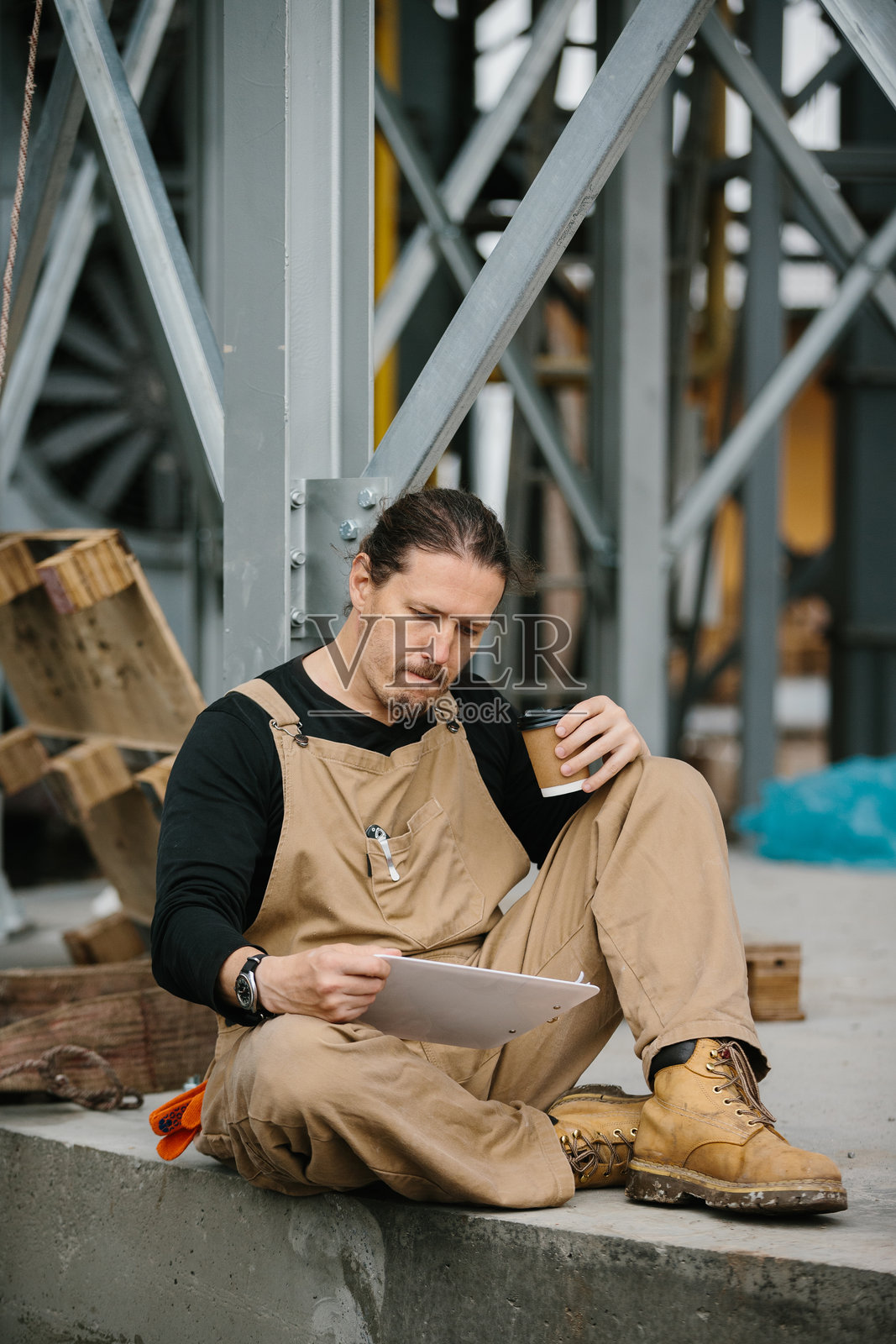 装配工人在建筑工地上坐着,喝咖啡并查看文件。照片摄影图片