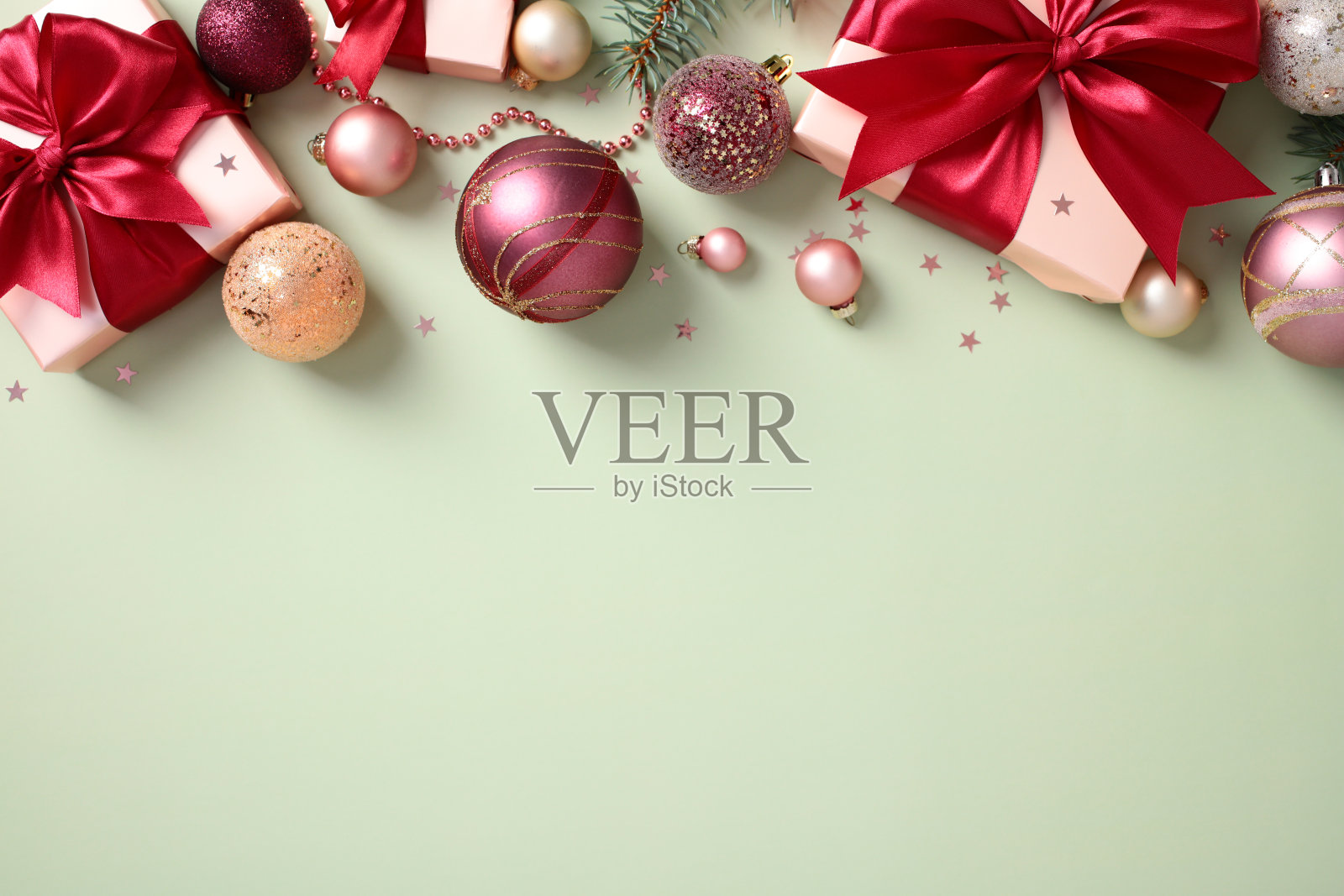 粉色礼物上装饰着红色丝带蝴蝶结、粉色球饰、闪光彩屑和松枝的圣诞平铺构图,背景为柔和的绿色。照片摄影图片