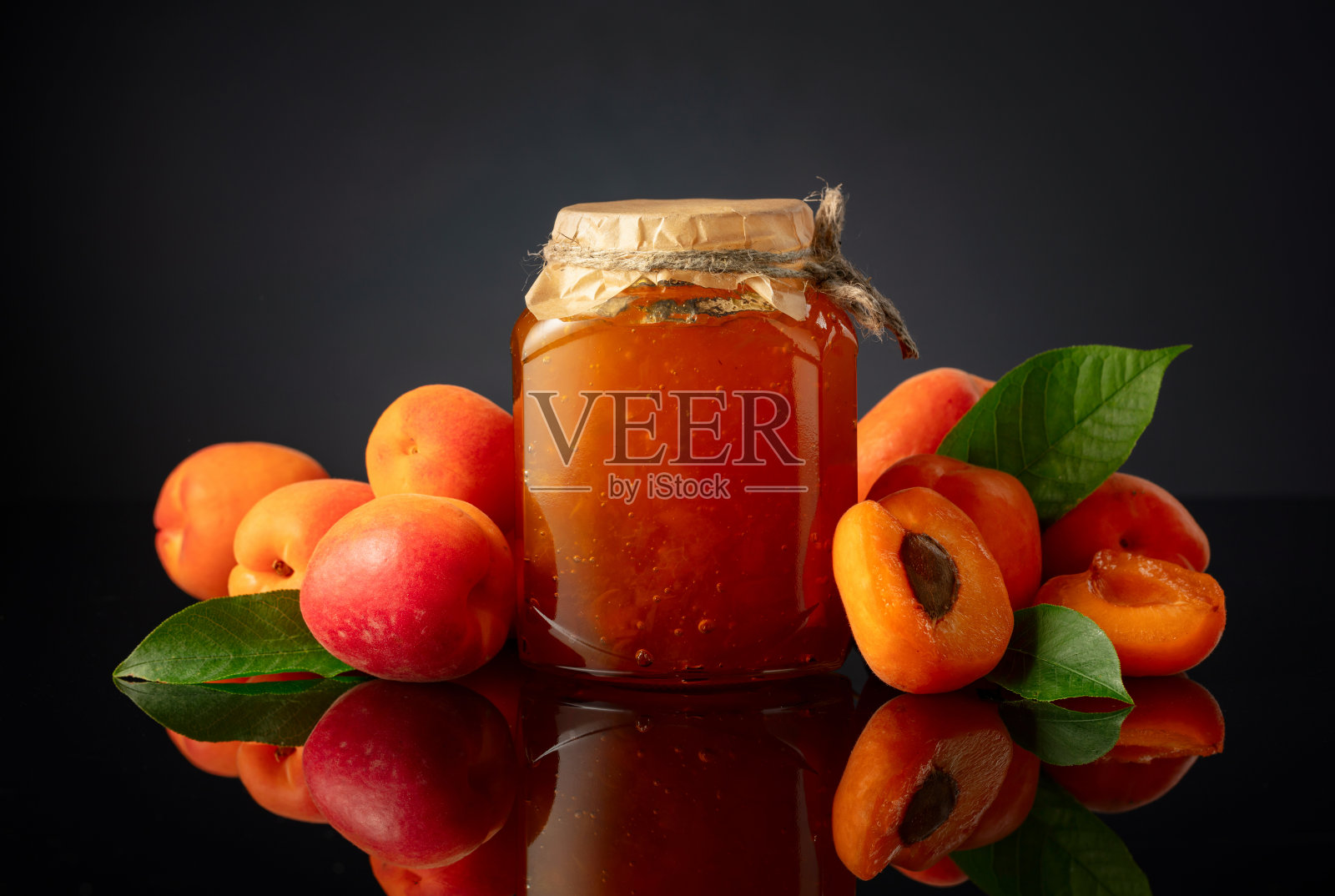 黑色反光背景上的玻璃罐杏脯果酱和新鲜水果。照片摄影图片