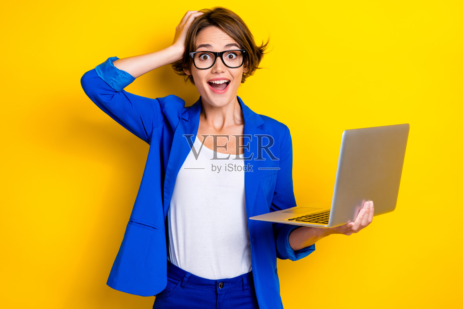 年轻的女性电商经理,棕色短发,手持笔记本电脑,困惑地摸着头,背景为黄色。照片摄影图片