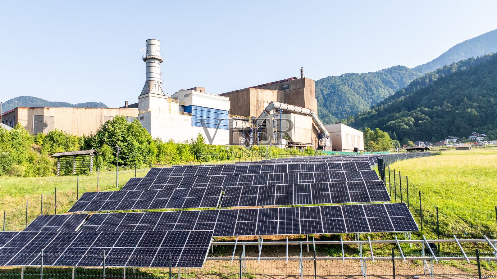 阳光明媚的日子里,电站的太阳能电池板与背景的山脉相映成趣照片摄影图片