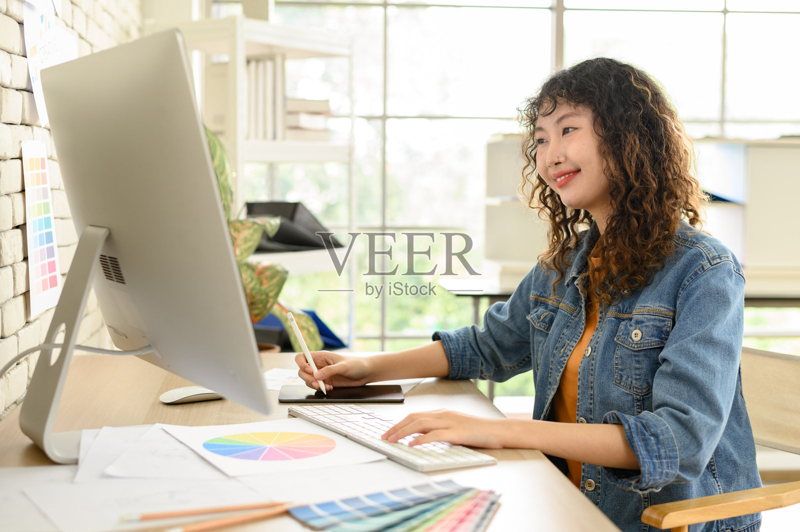 亚洲女性艺术家在图形平板上绘画。图形设计师在办公室工作。看向镜头。照片摄影图片