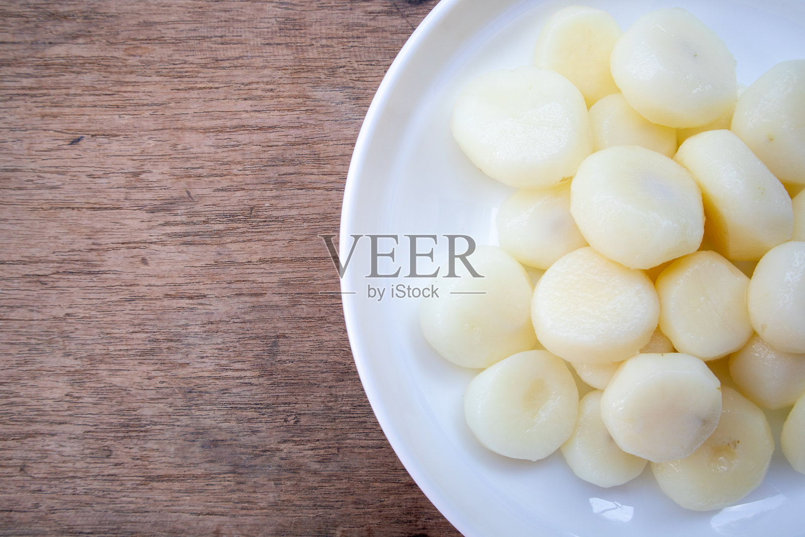 美味的去皮荸荠准备好可以食用,放在木桌上的白色盘子里。它富含营养和纤维。照片摄影图片