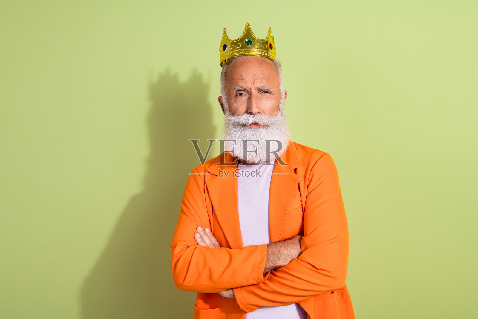 穿着橙色西装、双臂交叉的老年男性表演者,头戴金色王冠,背景为绿色。照片摄影图片