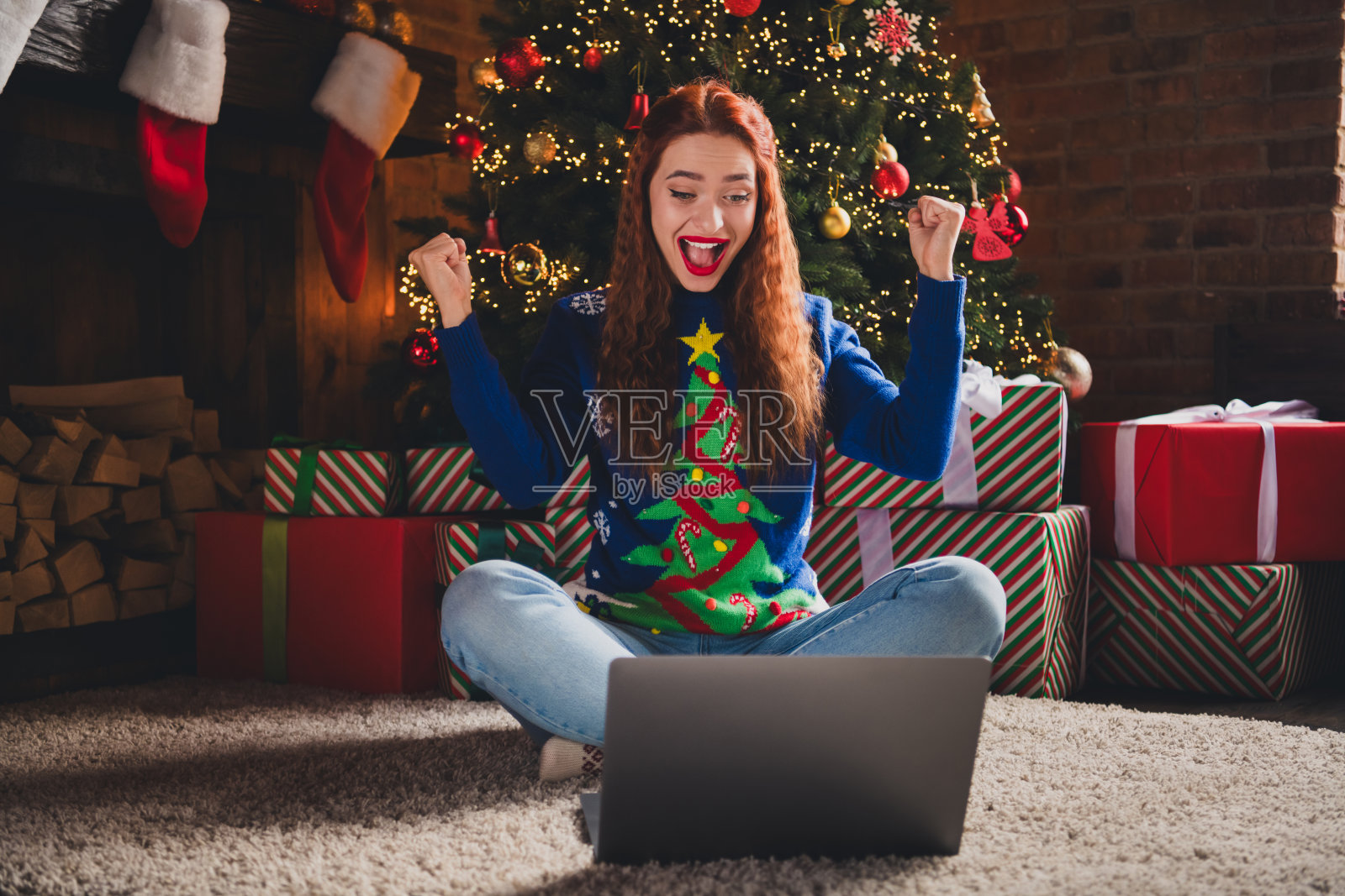 全身照,年轻女孩穿着蓝色圣诞服装,坐在现代舒适的室内,周围是圣诞派对装饰,手里拿着网本。照片摄影图片