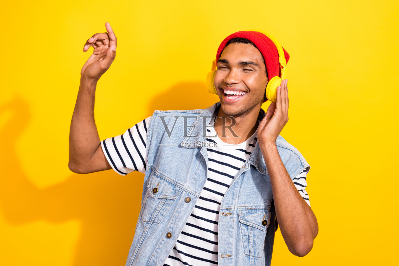 穿着时尚衣服的快乐时尚男士,享受美妙音乐,背景为黄色。照片摄影图片
