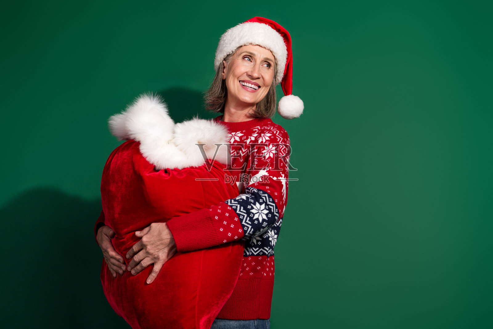 可爱的积极女性穿着红色印花衣服,手持大包礼物,背景为绿色。照片摄影图片