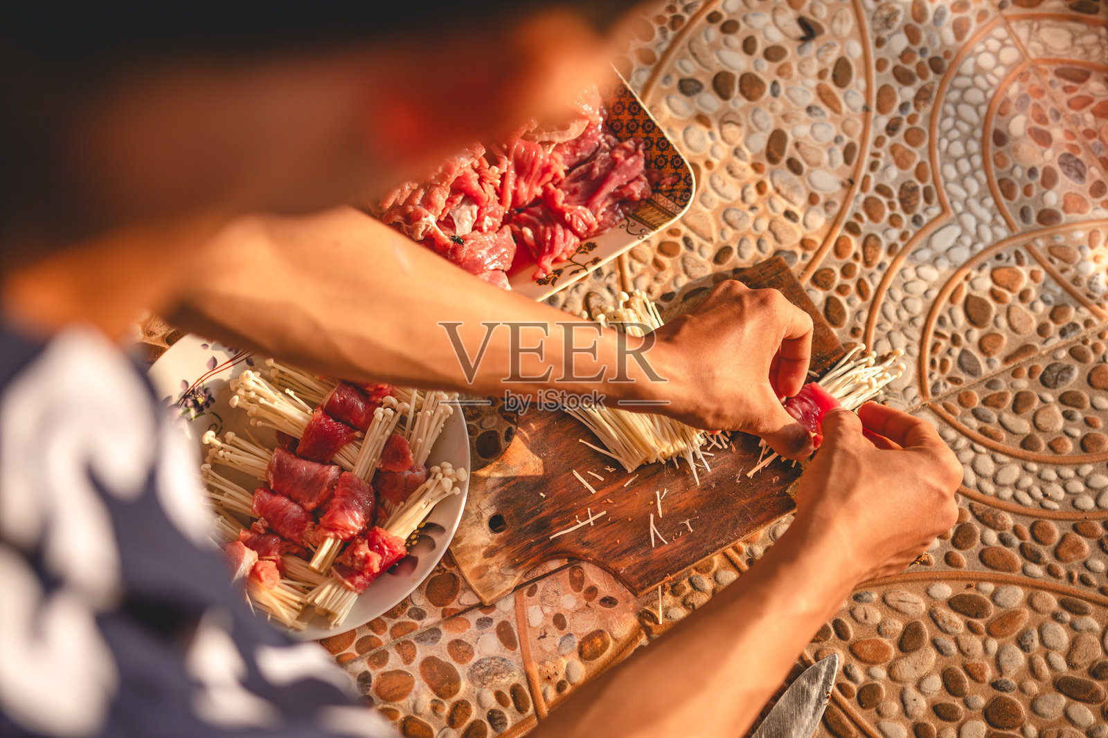 在切菜板上用锋利的刀切割金针菇。沿着准备好的肉的长度方向切割蘑菇。从左侧拍摄。照片摄影图片