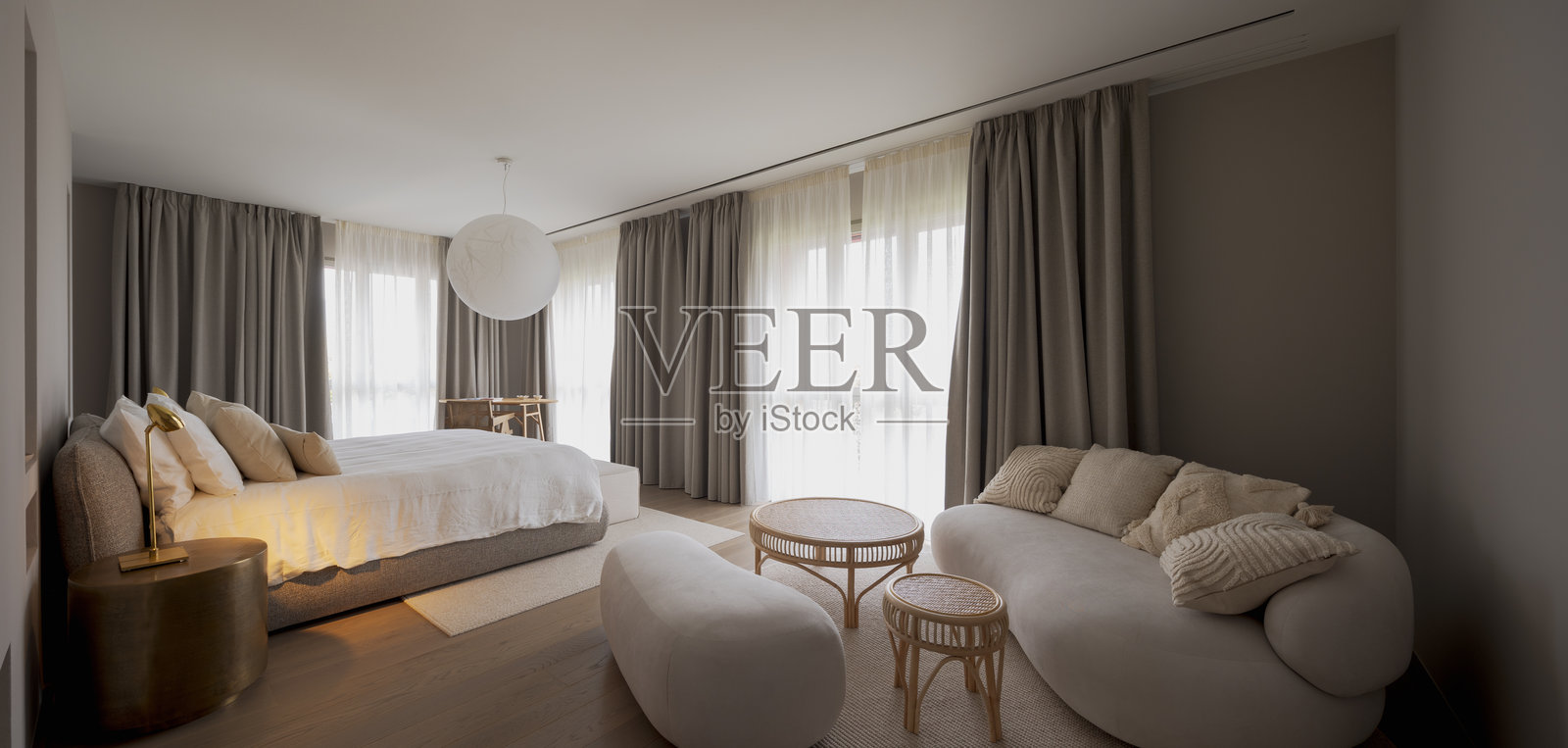 现代住宅中极简设计卧室的全景。房间内有一张大双人床、一个床头柜、一张浅色沙发和一张带椅子的书桌。照片摄影图片