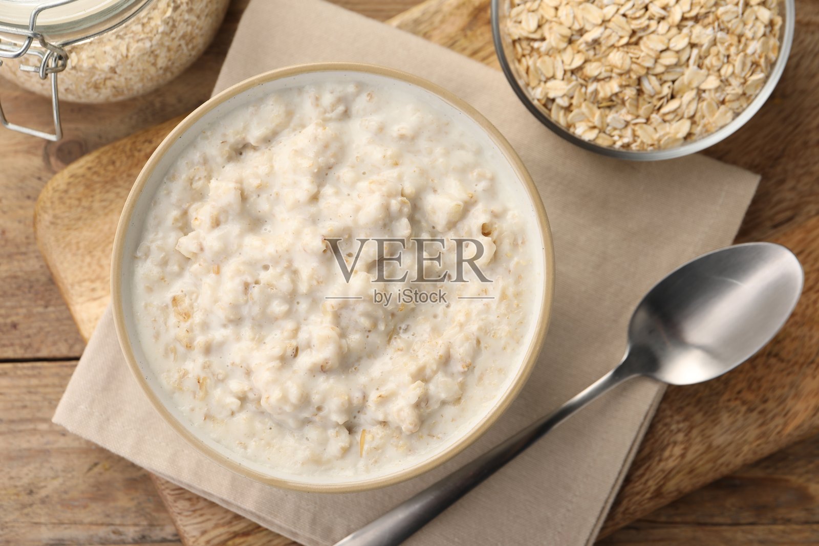 美味的煮燕麦粥放在碗中,旁边有燕麦片和勺子,平铺在木桌上照片摄影图片