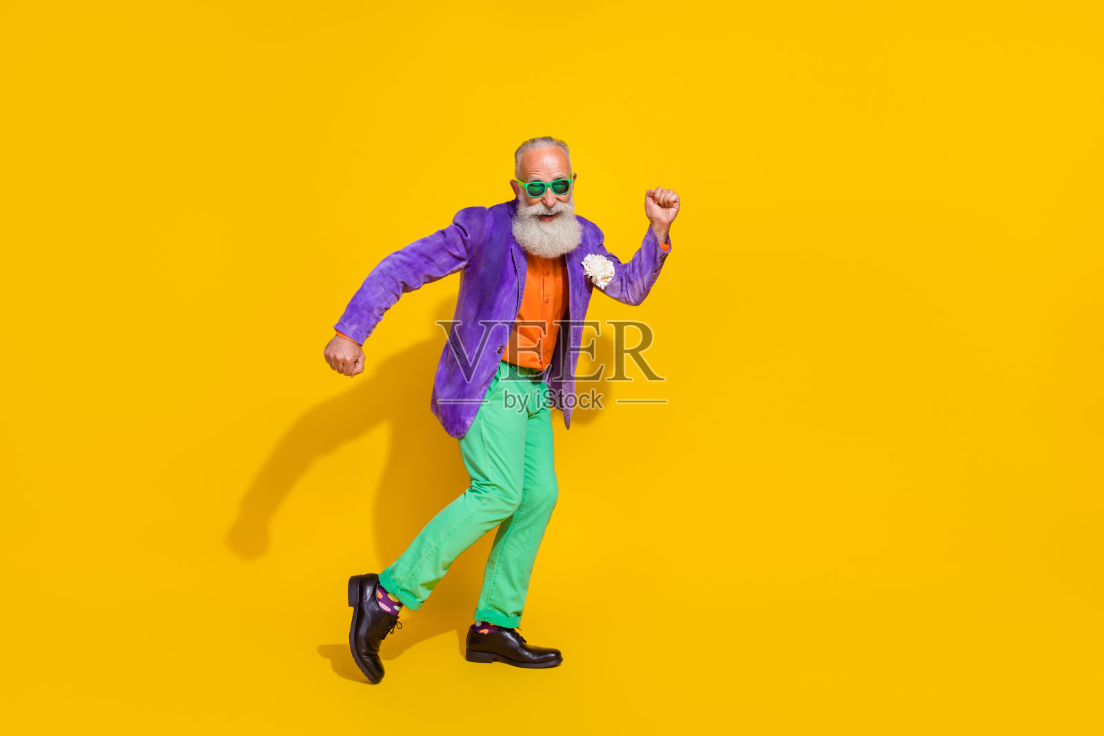 全身照,帅气的潮流爷爷心情愉快,充满活力地跳舞,穿着时尚的彩色衣服,背景为黄色。照片摄影图片