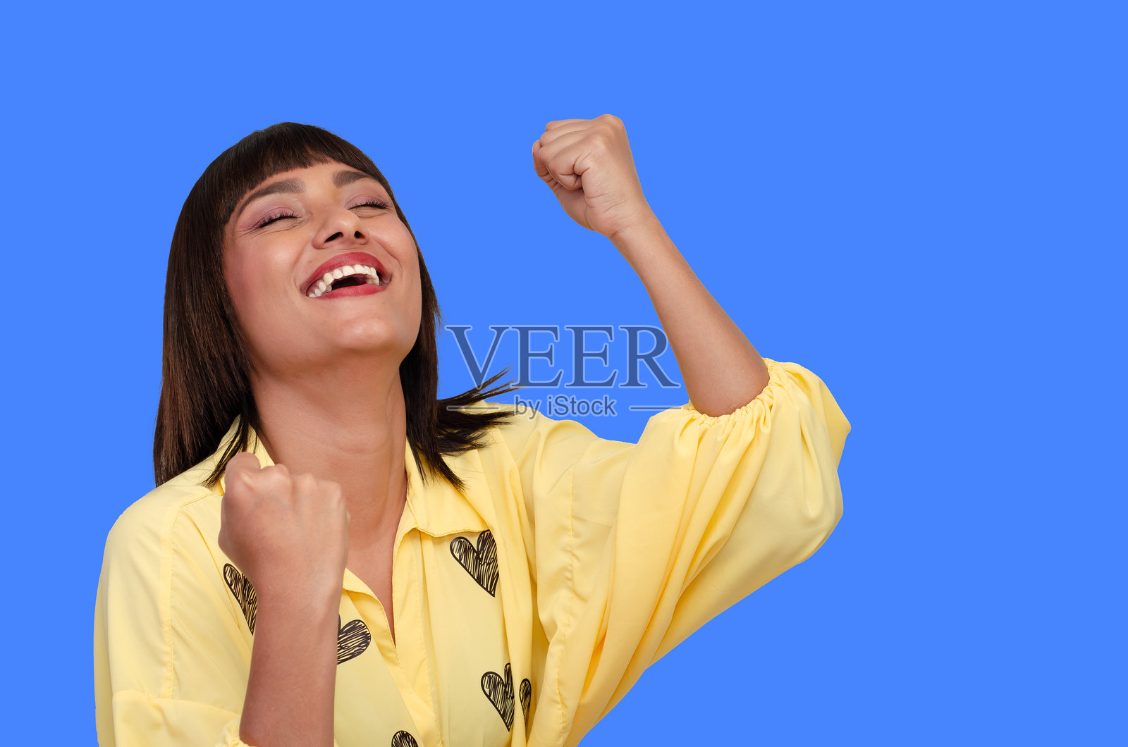 美丽快乐的年轻女性特写肖像,穿着色彩鲜艳的休闲服,短发,双臂高举,背景为蓝色。照片摄影图片