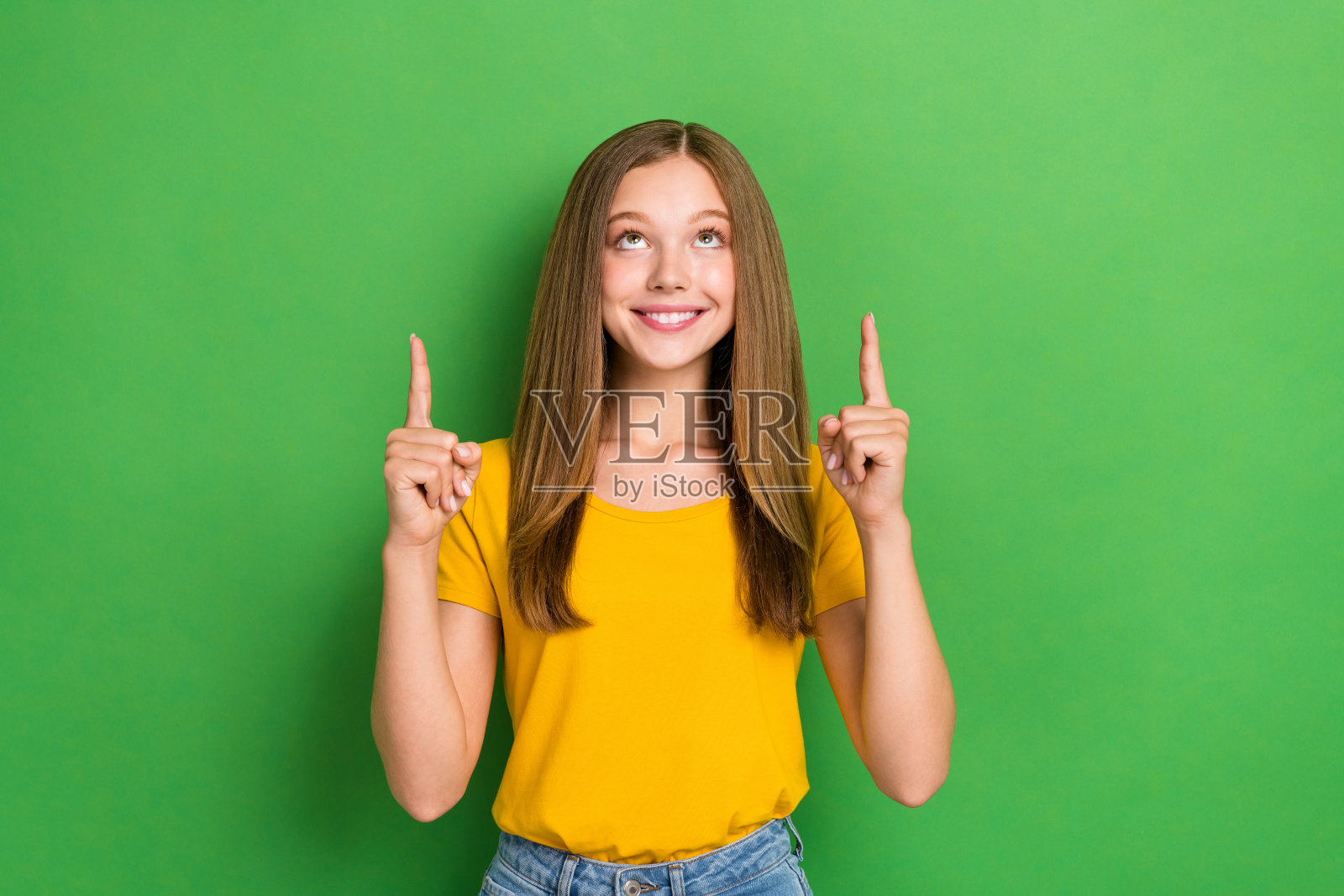 可爱的女孩露出灿烂的笑容,手指指向空白处,背景为绿色。照片摄影图片