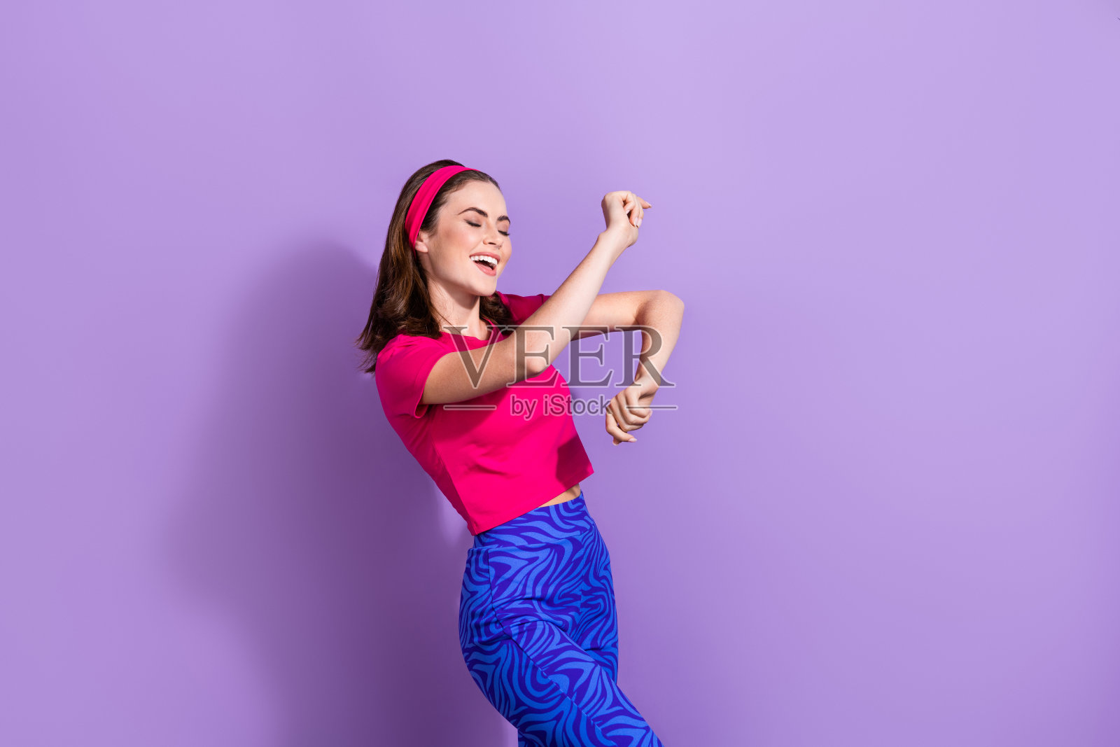 一位满脸喜悦、满意的女士闭着眼睛,享受着舞蹈,双手做出动作,背景为紫色。照片摄影图片