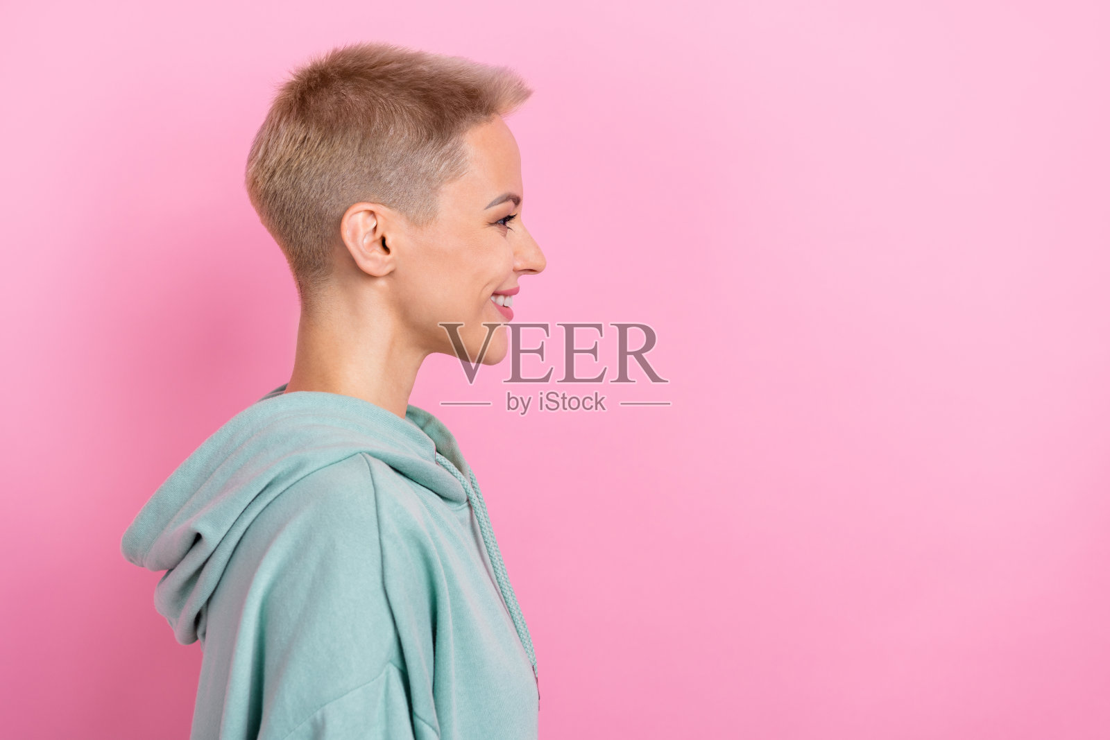 时尚的年轻女孩在粉色背景前微笑,穿着时尚的卡其色衣服,面带灿烂的笑容,目光空灵。照片摄影图片