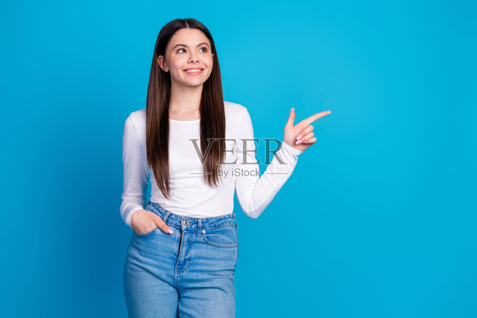 漂亮的少女穿着时尚的白色服装,指着空旷的地方,背景为蓝色。照片摄影图片