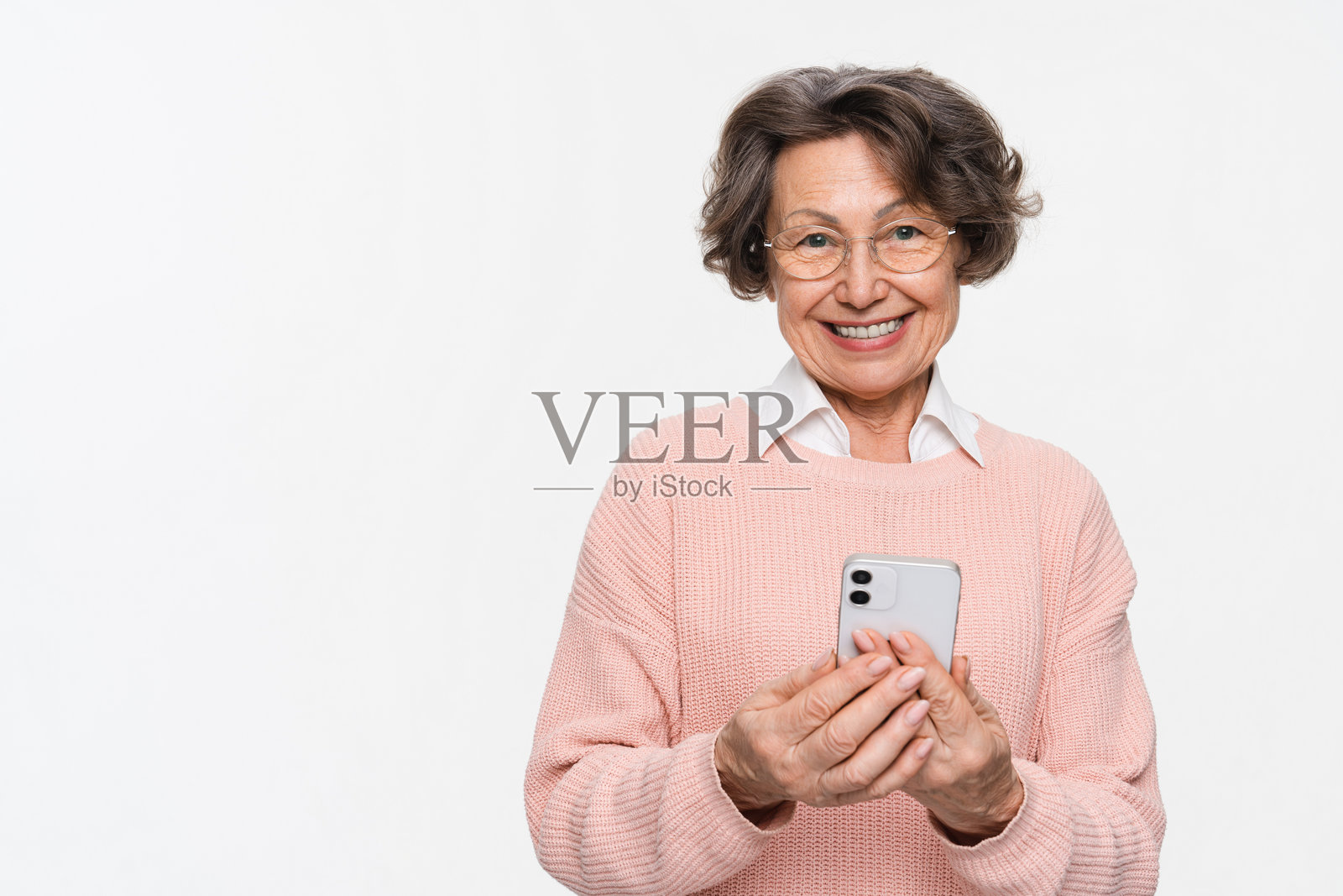 微笑的老年女性手持手机,背景为单色。科技概念照片摄影图片