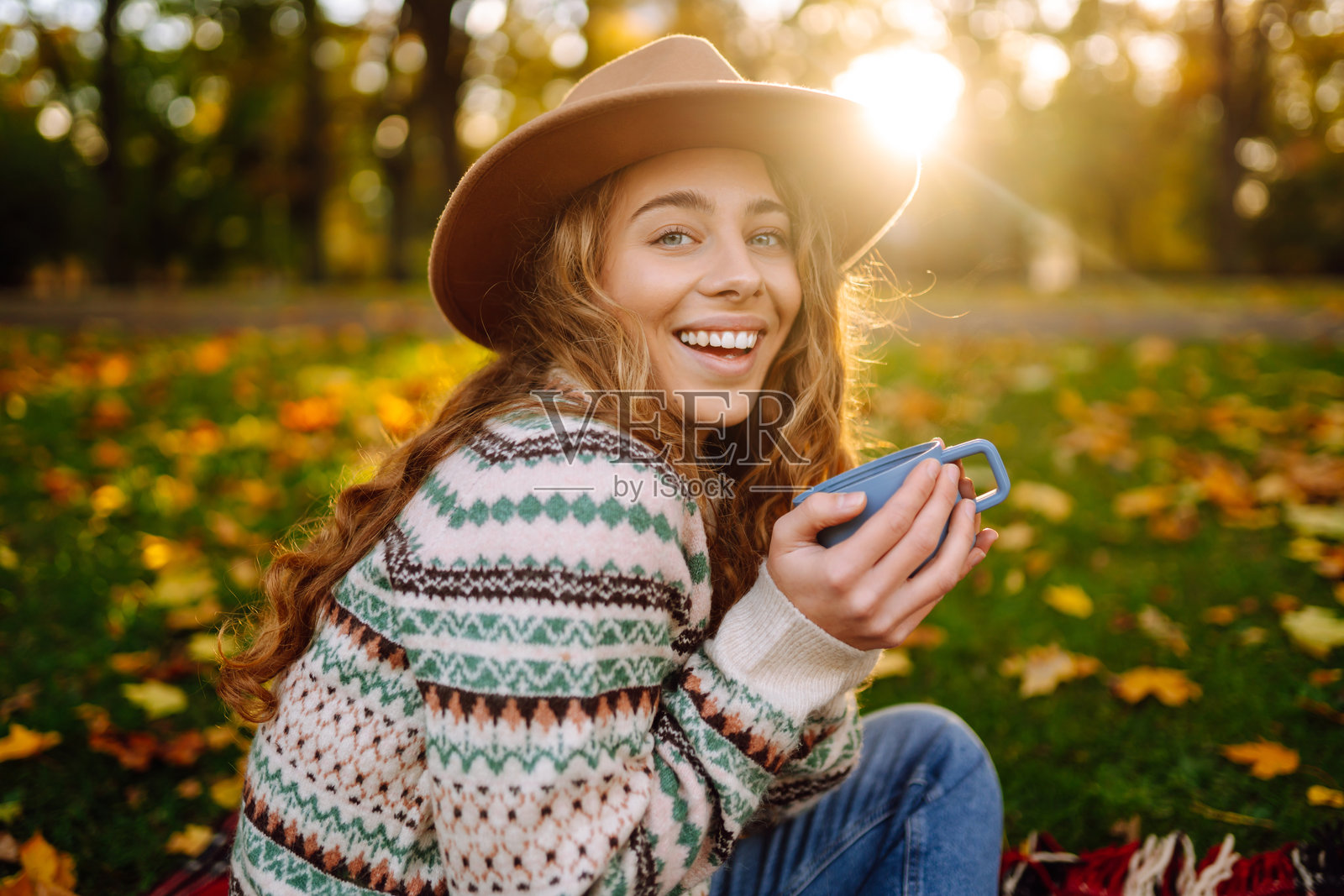 秋天的公园里,年轻女性在温暖的饮品陪伴下,享受舒适的下午野餐,四周环绕着五彩斑斓的落叶。照片摄影图片