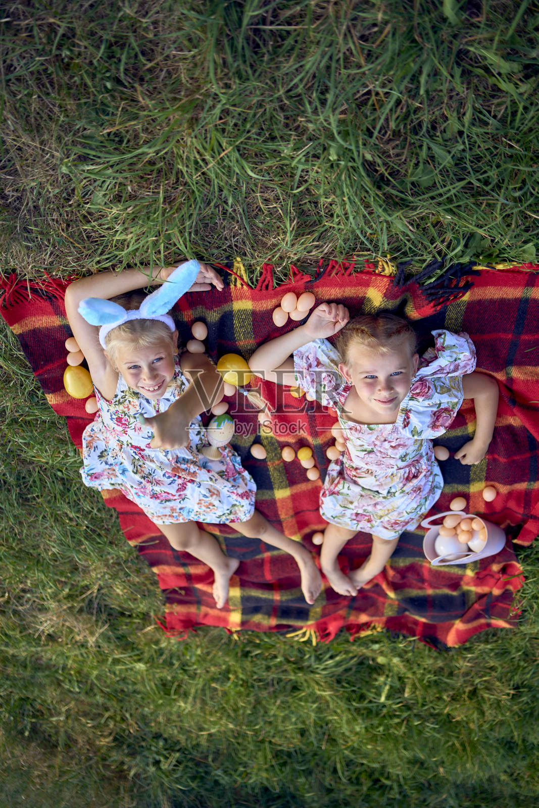 小女孩们,姐妹俩,在野餐毯上玩耍,手里拿着复活节彩蛋。照片摄影图片