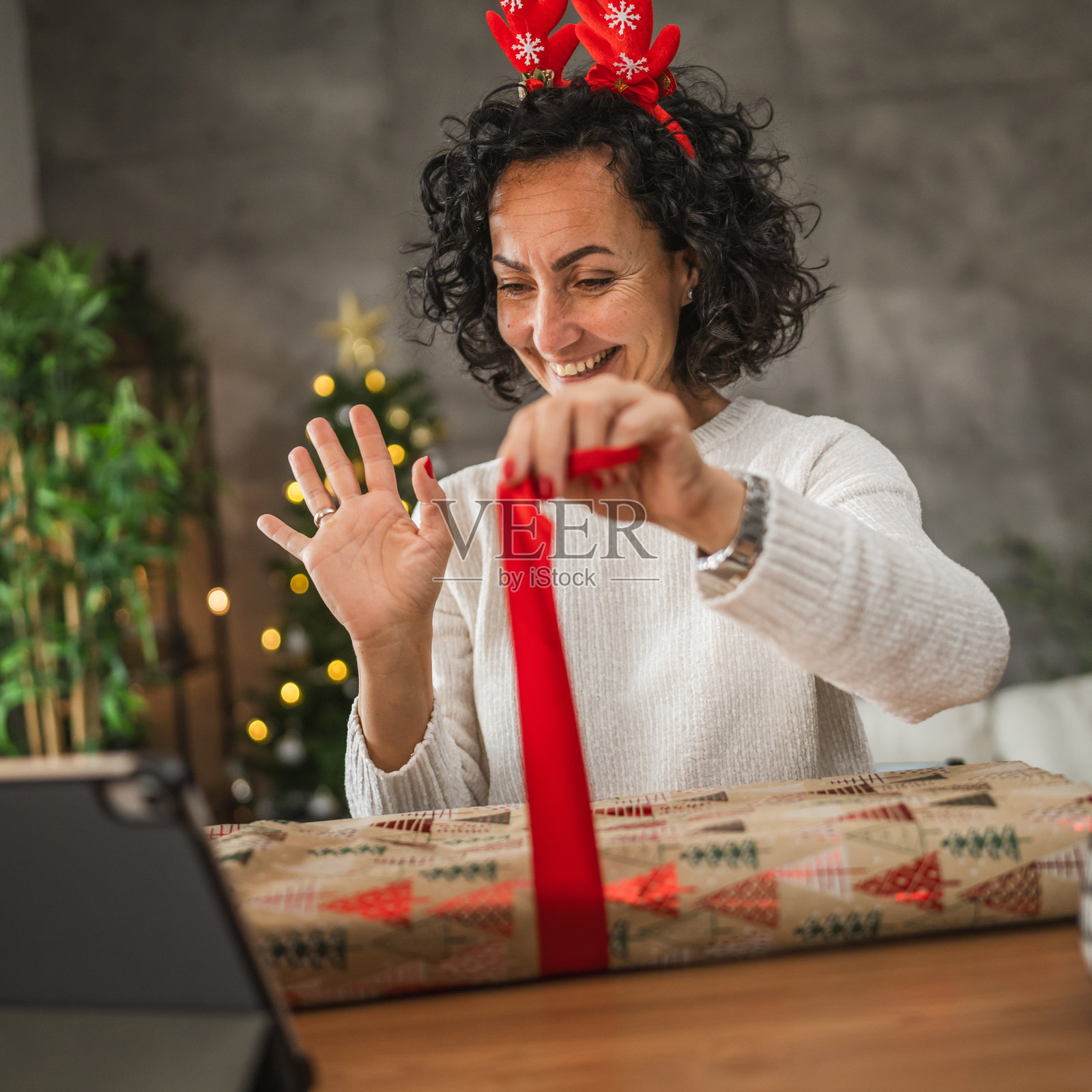 成熟的女性在视频通话中包裹礼物,节日气氛洋溢。照片摄影图片