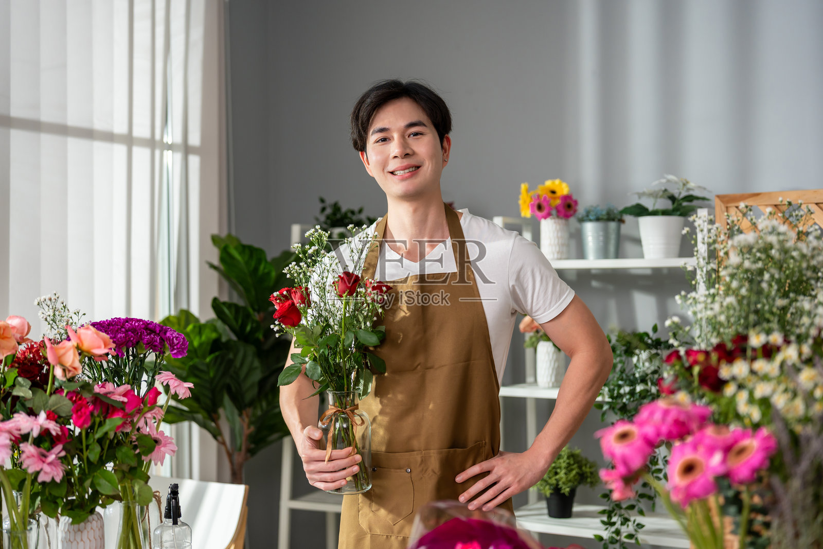 亚洲花店男花匠在花店里完成美丽的花束。这个迷人的小企业主看着镜头,同时为顾客包装花卉礼品。照片摄影图片