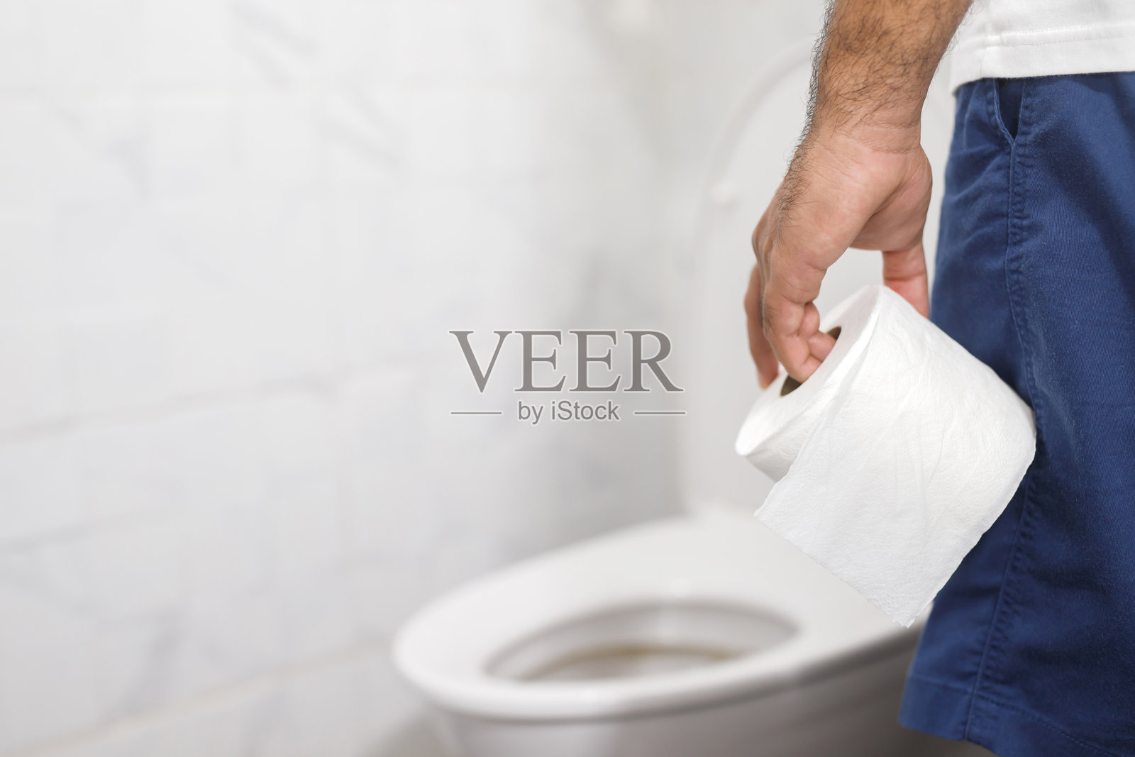 男子因腹泻而痛苦,手中握着卫生纸卷,坐在马桶前。卫生间里的便秘。治疗腹痛和卫生保健。照片摄影图片