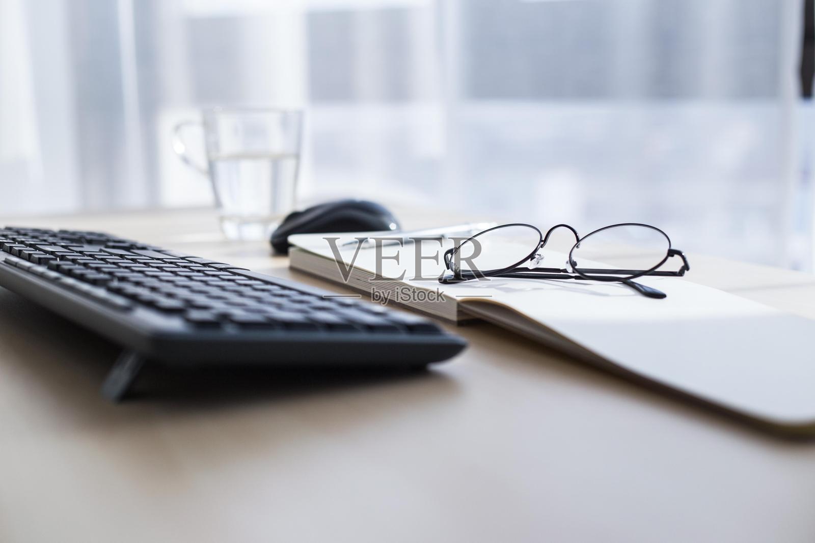 黑色键盘、鼠标、眼镜和笔记本放在家用办公室的木桌上照片摄影图片