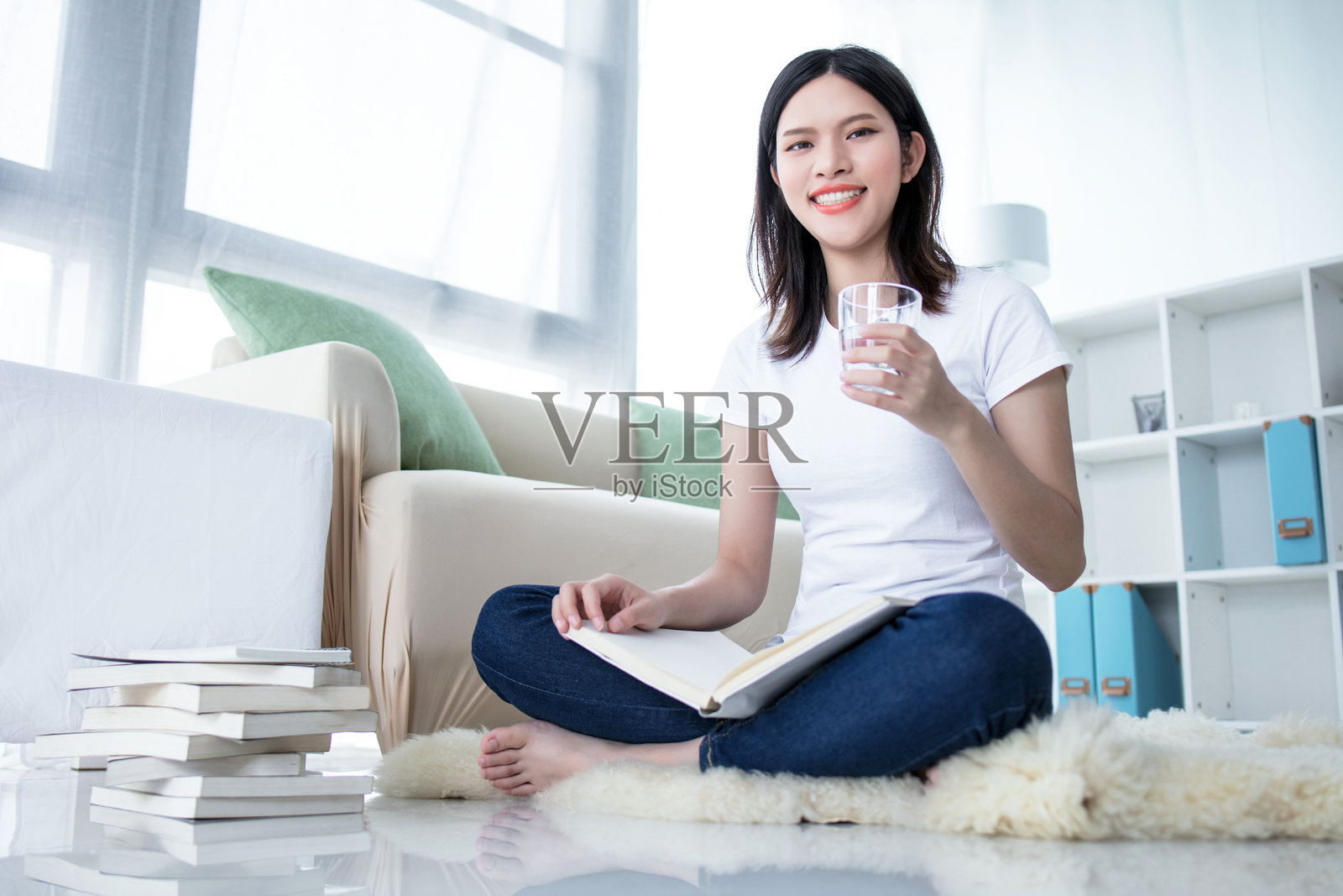 微笑着的小女孩坐着,双腿交叉,阅读一本书,背景为白色。照片摄影图片