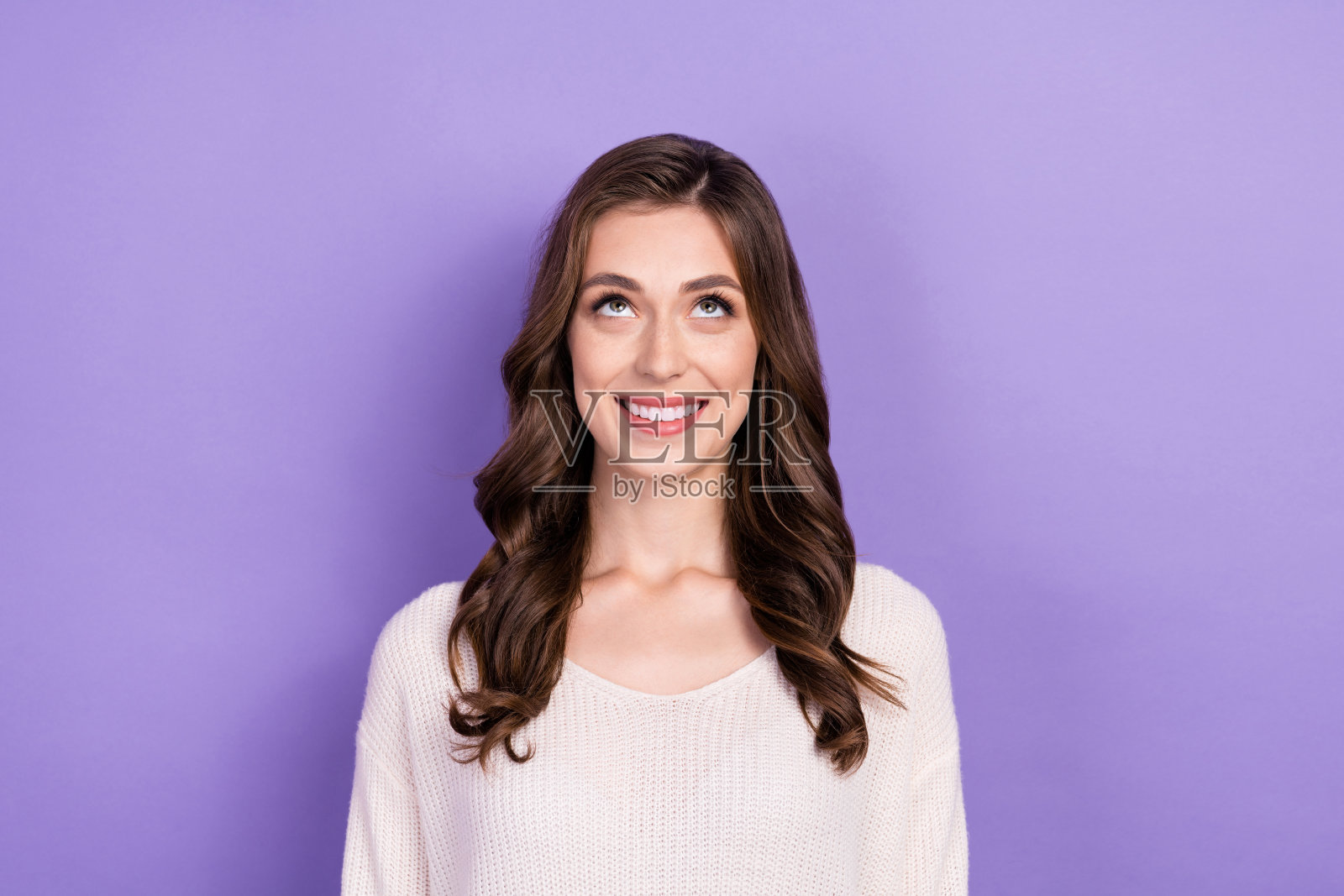 一位积极心态的棕发女士,露出灿烂的微笑,仰望着有用的信息,背景为紫色。照片摄影图片