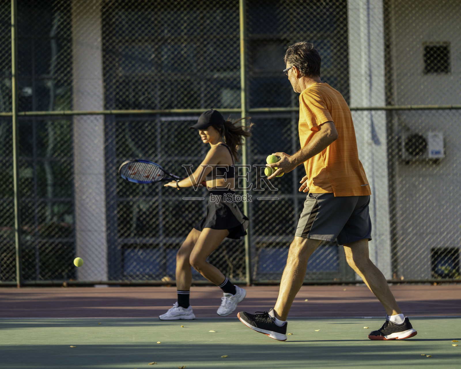 资深男性网球教练正在硬地球场上教女性网球运动员打网球。照片摄影图片