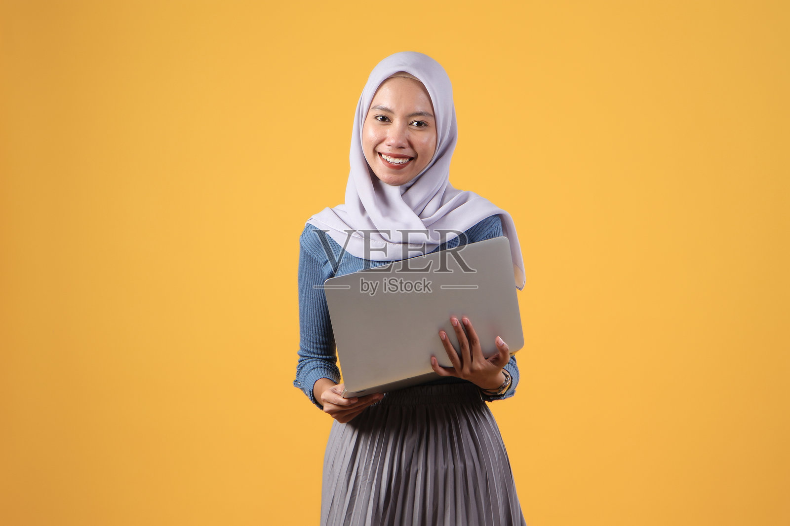 快乐的亚洲印尼穆斯林妇女在黄色背景上手持笔记本电脑照片摄影图片