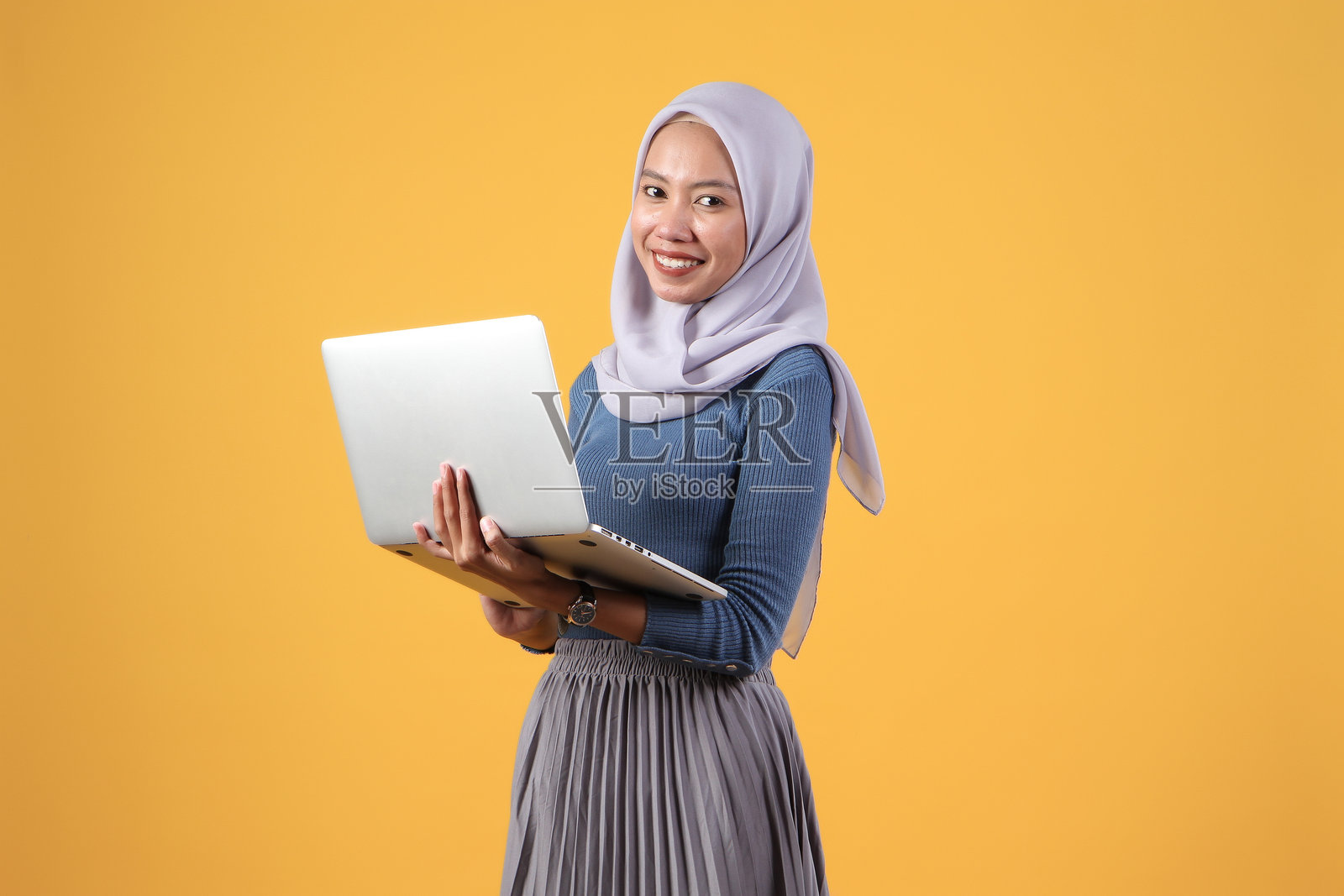 快乐的亚洲印尼穆斯林妇女在黄色背景上手持笔记本电脑照片摄影图片