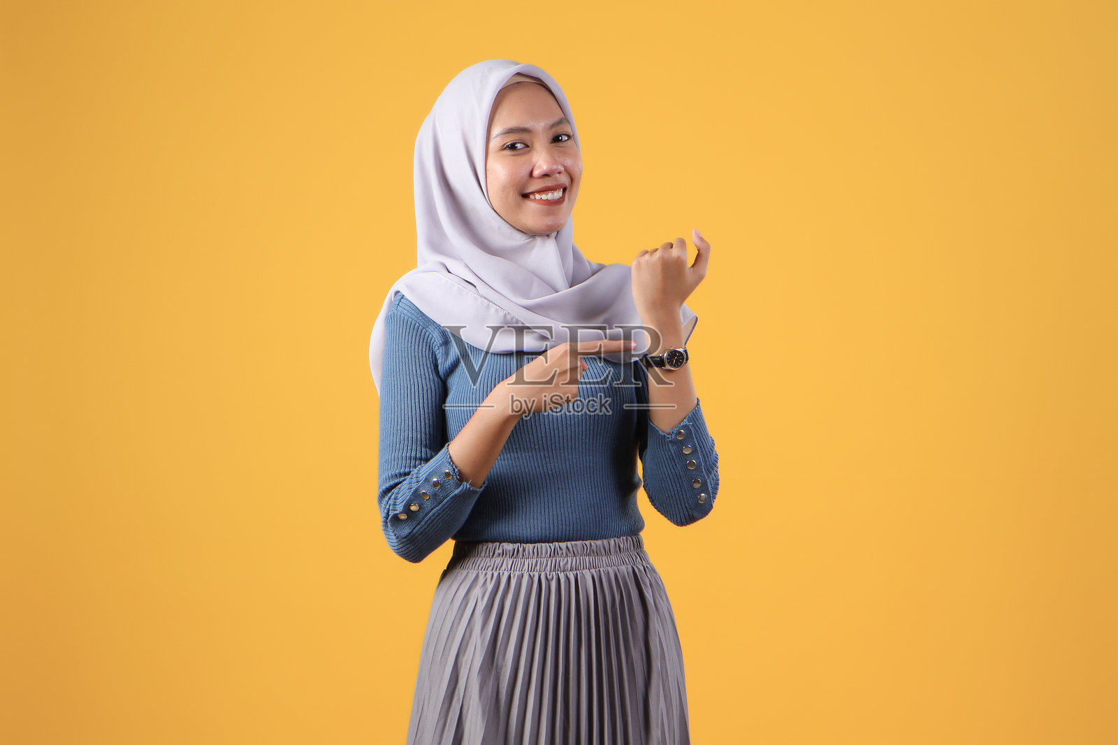 快乐的亚洲印尼穆斯林妇女在黄色的孤立背景上使用腕表照片摄影图片