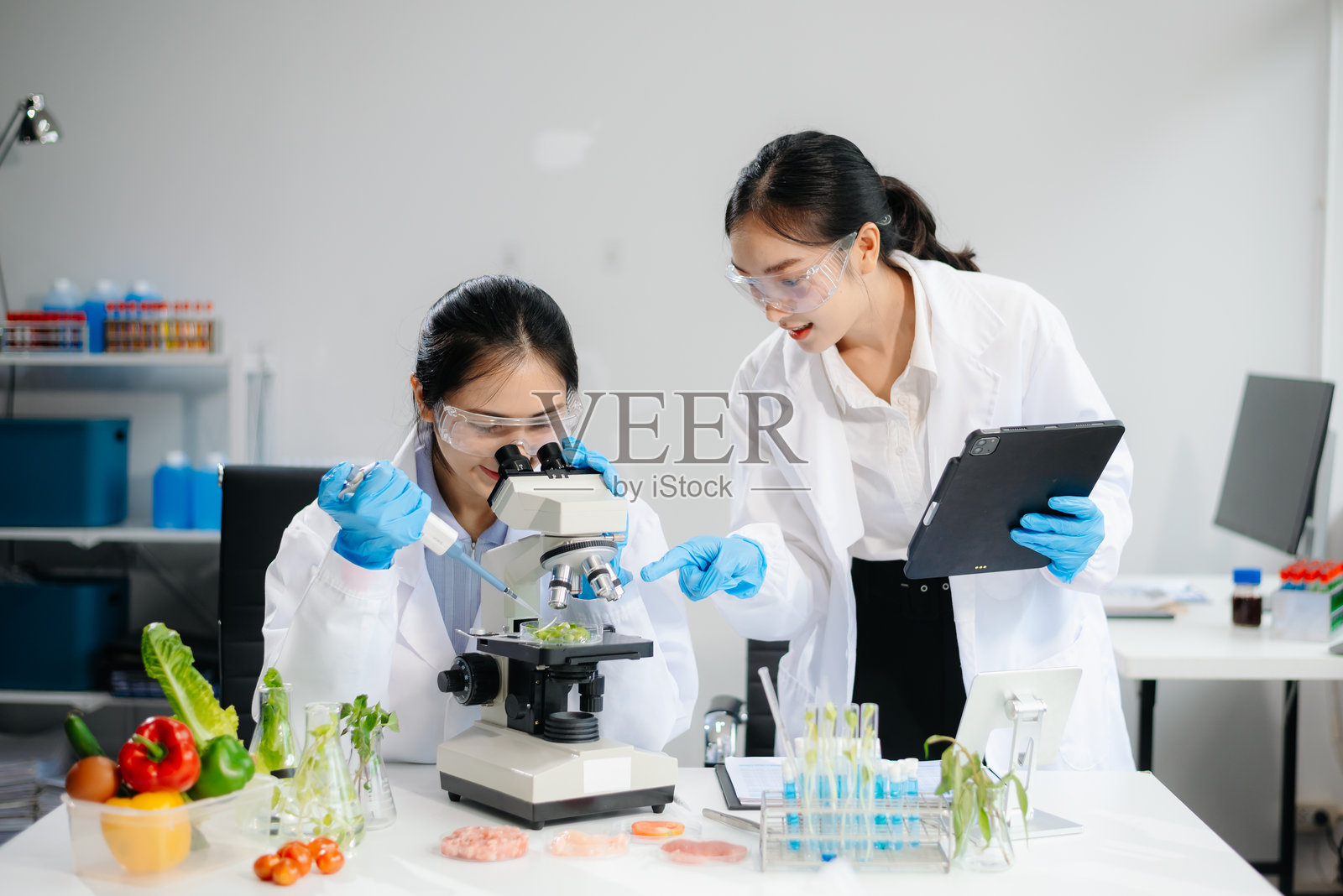 两位亚洲科学家在实验室中使用显微镜和实验设备进行食品研究,展示食品科学的创新。照片摄影图片