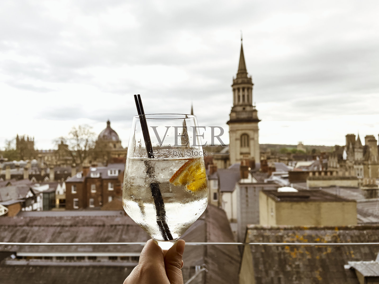 一只手握着鸡尾酒,俯瞰牛津的历史天际线,这是一杯清爽的饮品,伴随着城市标志性的建筑。照片摄影图片