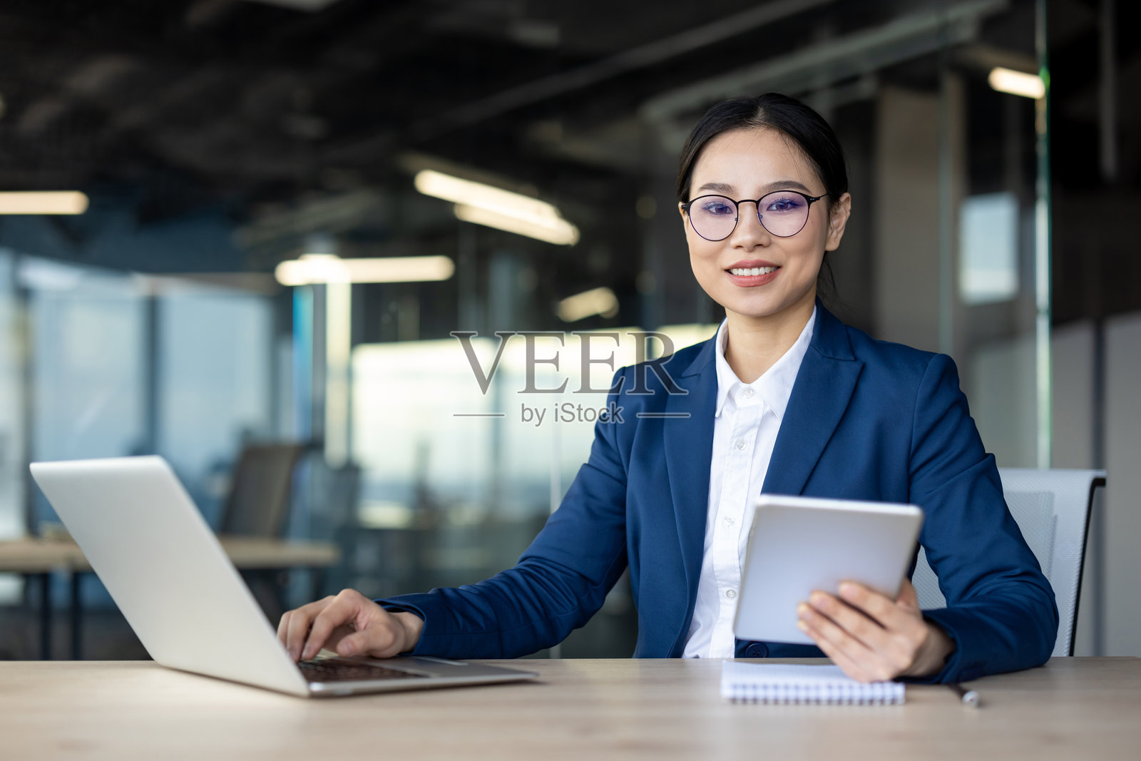 自信的亚洲女商人在现代办公室使用笔记本电脑和平板电脑工作照片摄影图片