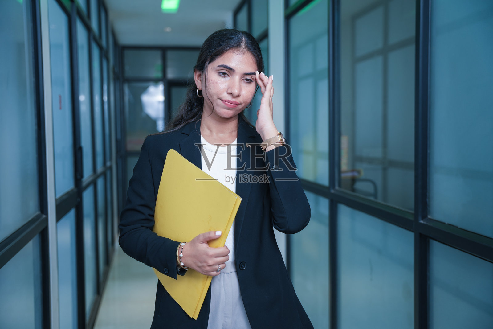 年轻的印度女商人在办公室走廊里用手触摸额头,手中拿着报告或文件。过度劳累的女性,感到压力的概念。照片摄影图片