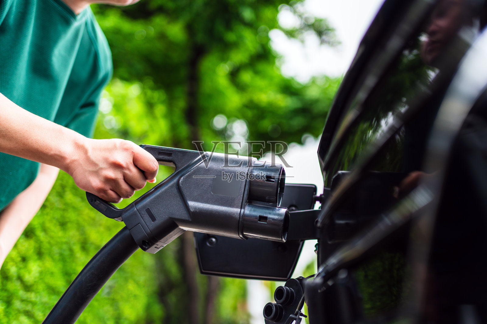 户外能源站区域特写:一只手握着电动车直流充电器插头。电动车充电插头代表环保理念。可持续能源与经济交通的概念。照片摄影图片
