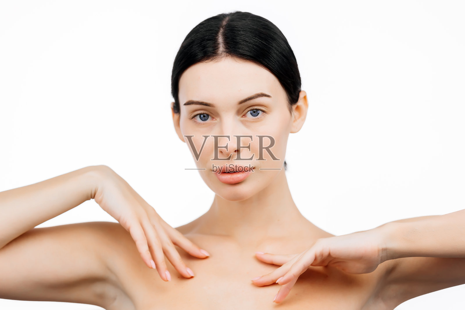 一位年轻女性在白色背景的工作室中轻轻触摸她完美无瑕的肌肤。她的表情传达出快乐与和谐,突显了她的魅力和精致的外貌。照片摄影图片