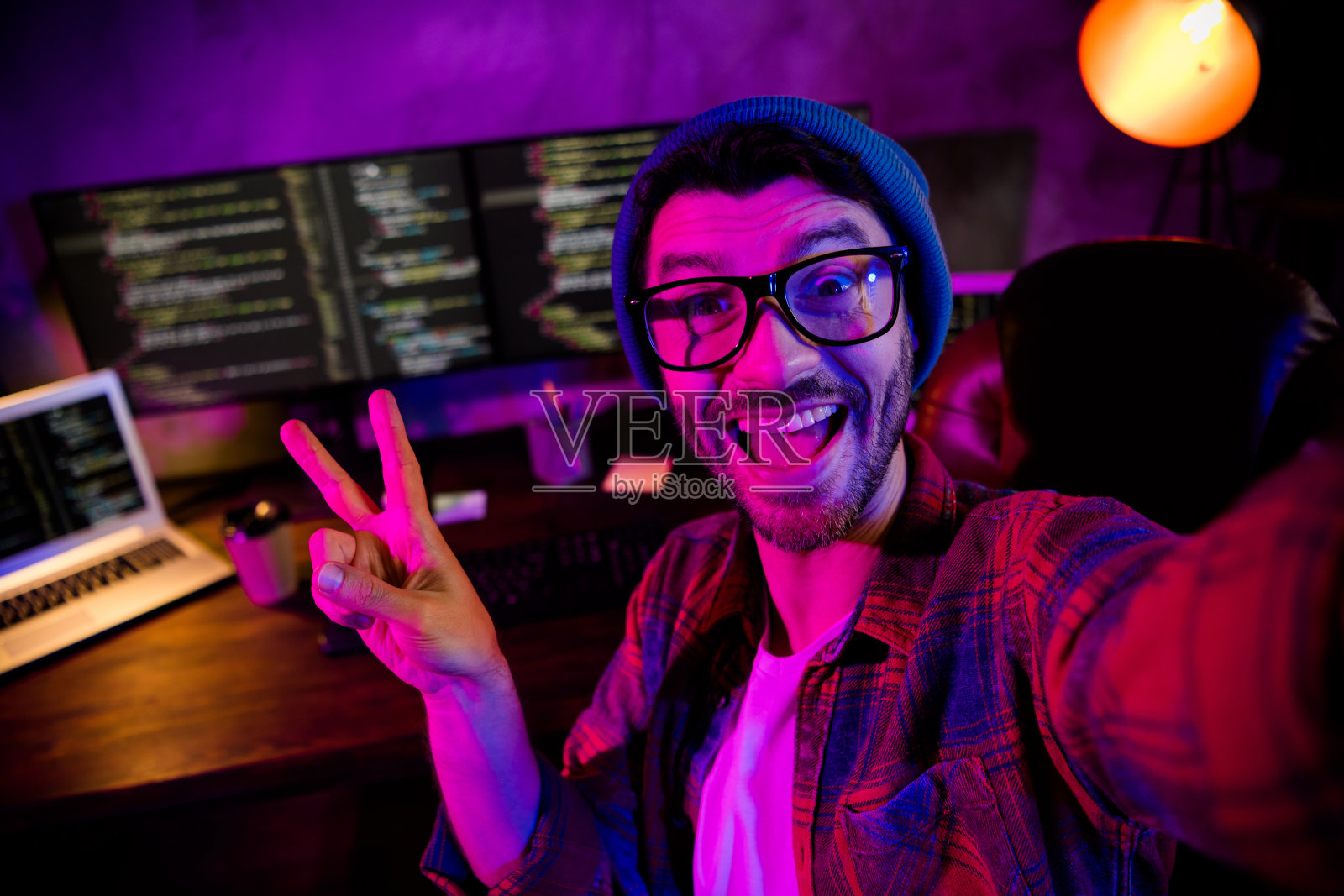 兴奋有趣的程序员戴着眼镜录制视频,在工作场所展示V字手势照片摄影图片