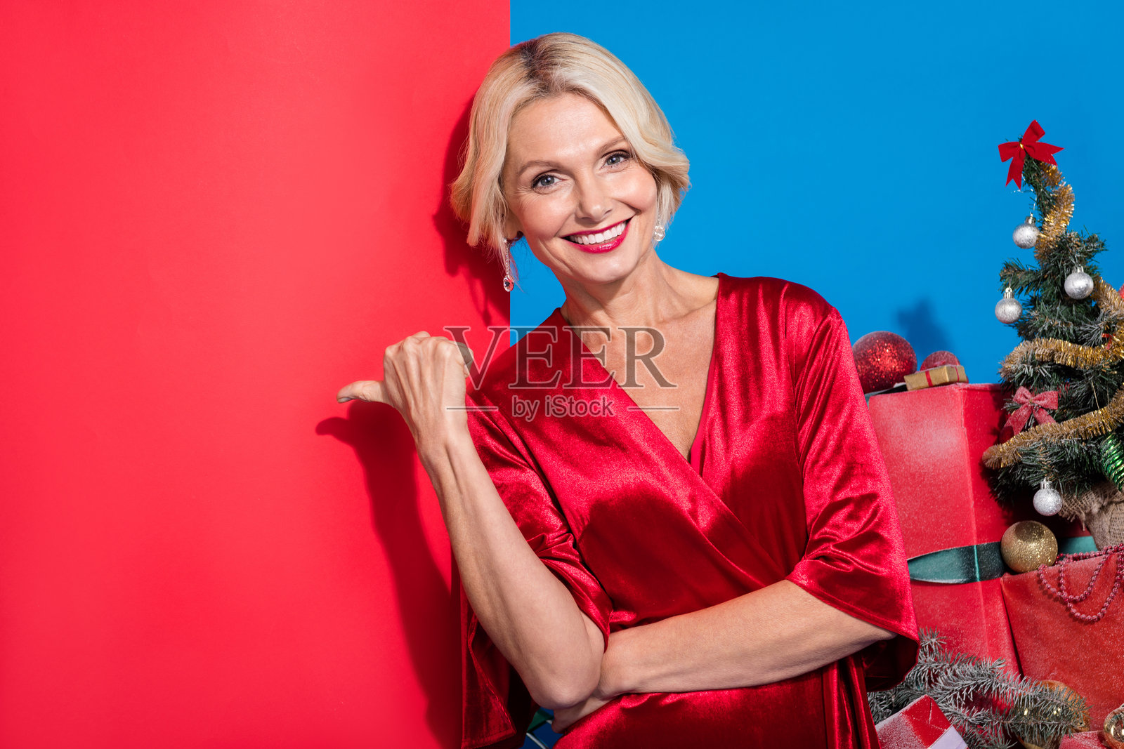 穿着闪亮红色衣服的迷人女士在蓝色背景下指向空白处。照片摄影图片